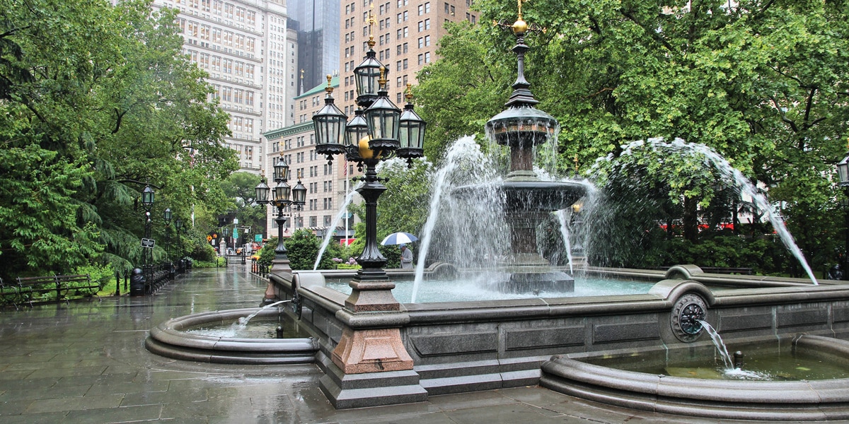 Ornate Stone and Metal Fountain With Several Spouts Sits in a Paved Stone Courtyard